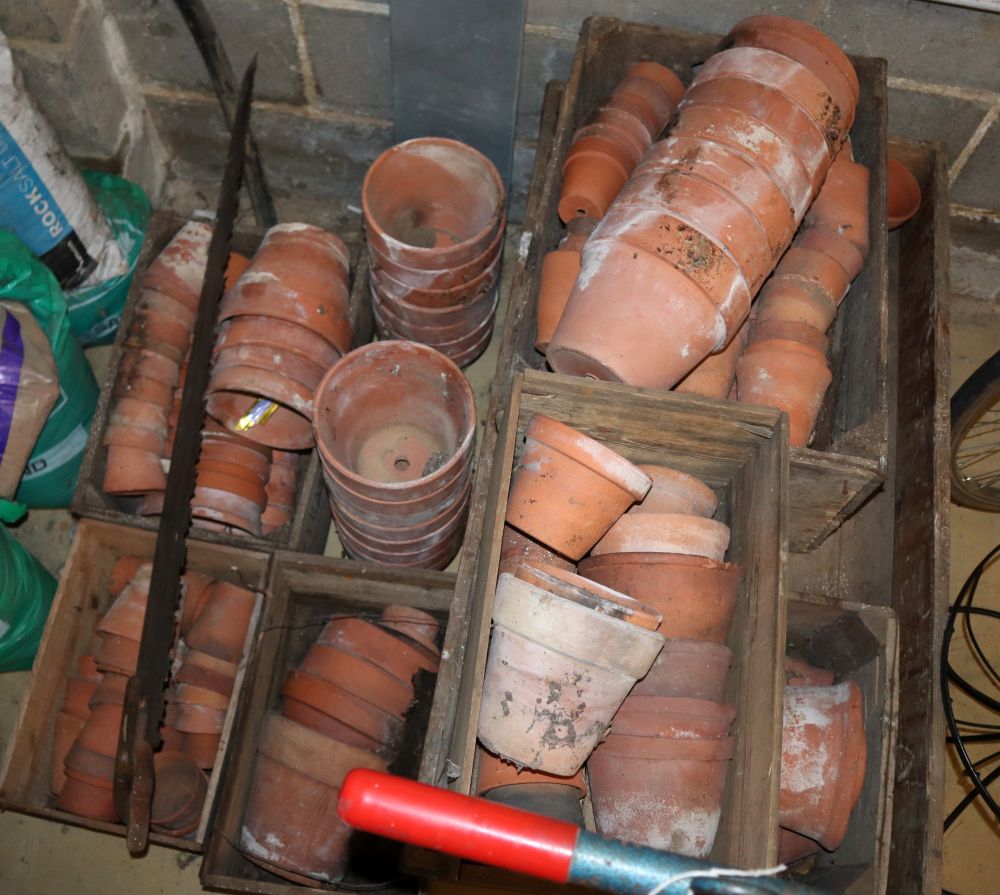 A large quantity of assorted terracotta plant pots, together with a garden trolley and a saw, largest pot 15cm high